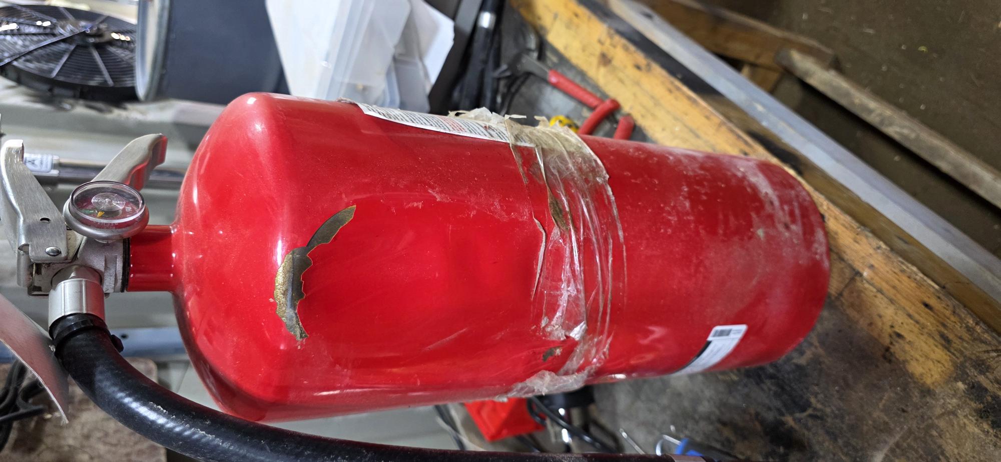 Dented fire extinguisher cylinder with paint removed and tape wrapped around the body — real field finding from Northern Alberta